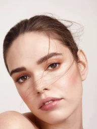 Close-up beauty portrait of a woman with styled brown hair and soft natural makeup against a plain background