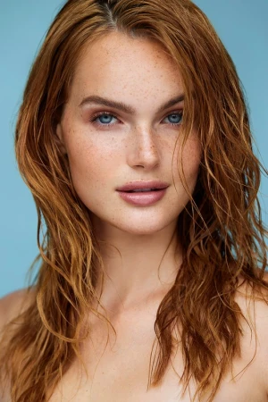 Close-up portrait of a woman with red hair, blue eyes, and freckles against a solid blue background styled by Destiny Venice