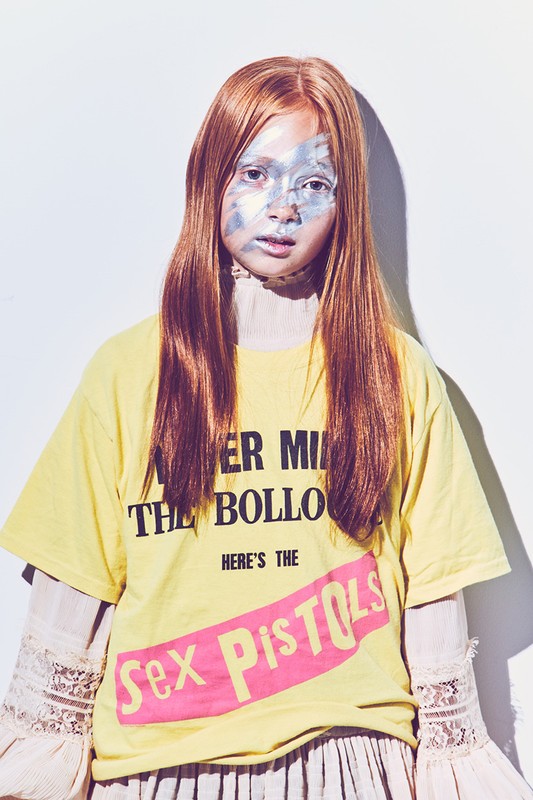 Young female model with face paint, wearing Sex Pistols t-shirt in a bright studio, showcasing alternative fashion and makeup.