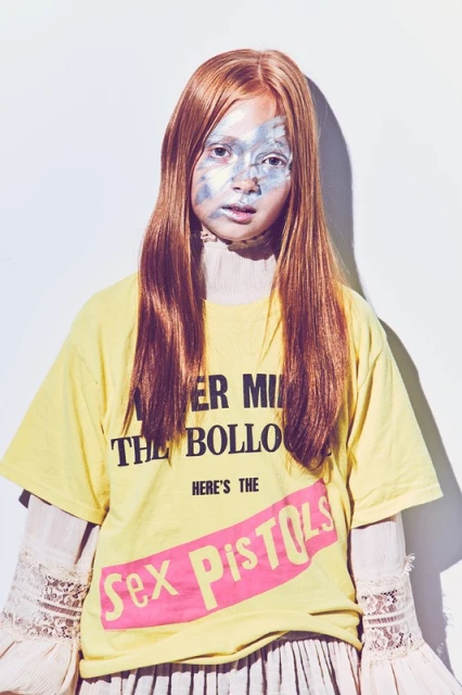 Young female model with face paint, wearing Sex Pistols t-shirt in a bright studio, showcasing alternative fashion and makeup.