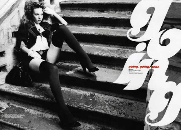 Model seated on stone outdoor steps wearing dark clothing and thigh-high stockings with makeup by Devra Kinery.