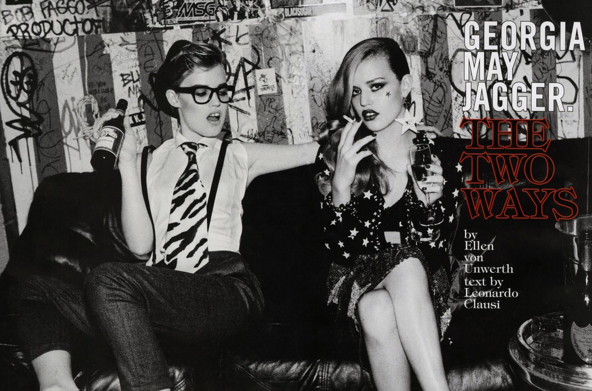 Black and white fashion editorial shot of two women posing on a couch, holding drinks, wearing stylish outfits, and smoking a cigarette.