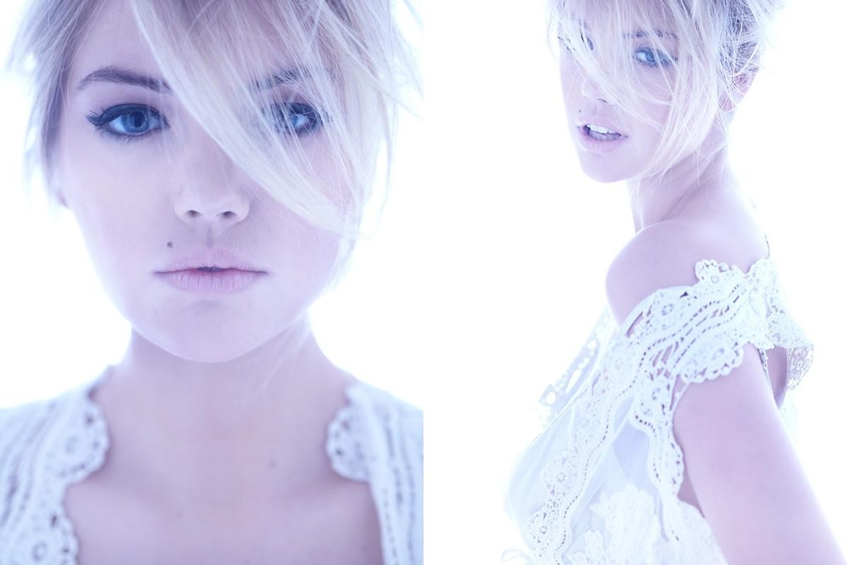 Close-up shot of a fair-skinned adult female fashion model with blonde hair and blue eyes, wearing a white lace top, on bright white.