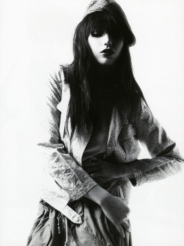 Young woman in jacket and cap poses in a studio fashion shot. Dark hair and eyes. Monochrome image. Studio lighting. Youth fashion concept.