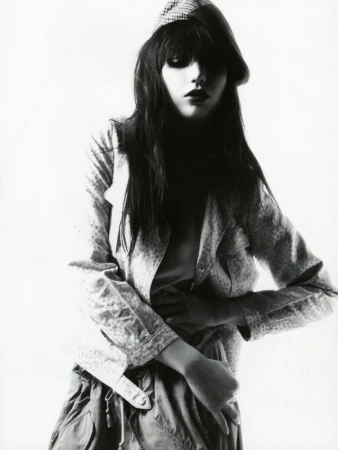 Young woman in jacket and cap poses in a studio fashion shot. Dark hair and eyes. Monochrome image. Studio lighting. Youth fashion concept.