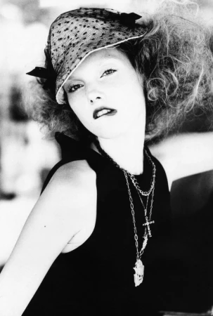 Black and white portrait of a woman wearing a patterned hat and layered necklaces with make-up by Devra Kinery.
