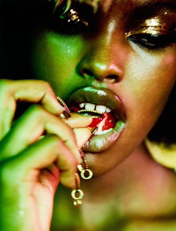 Close-up studio shot of an African-American female with glitter makeup putting food into her mouth with a gold chain around her finger.