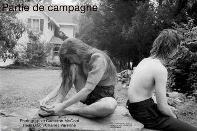 Black and white editorial photograph of a seated young woman touching her bare feet beside a shirtless person outdoors.