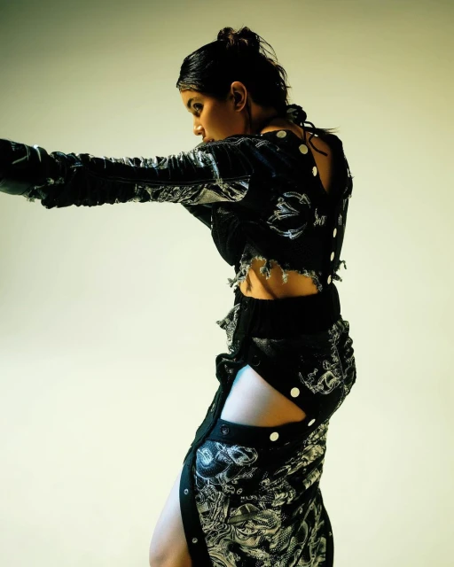 A fashionable woman poses in black-and-white patterned crop top and skirt against a graduated yellow background in a studio shot.