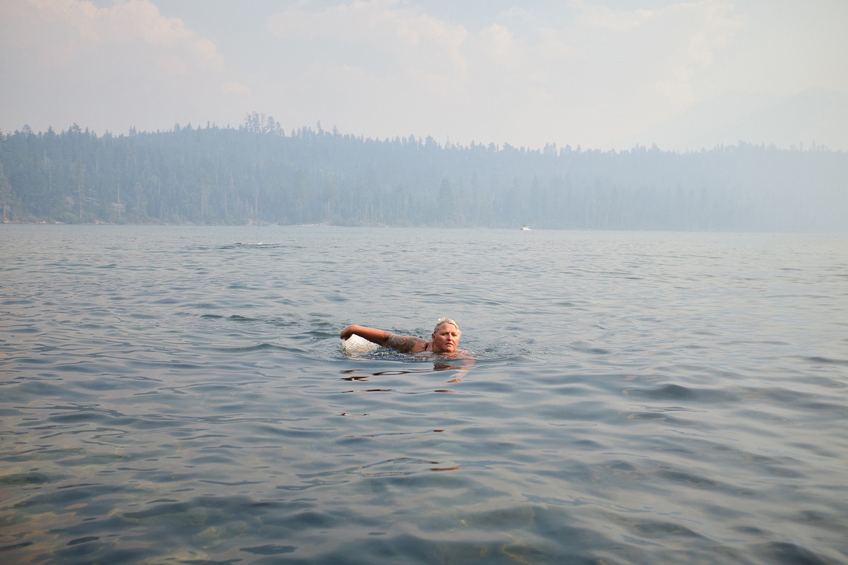 A person swimming in a vast, calm lake under a hazy sky with distant tree-lined shores