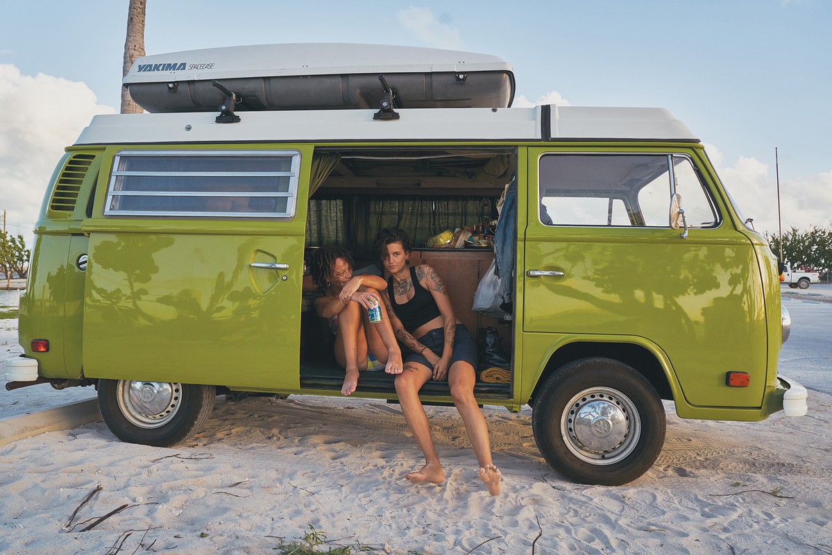Two tattooed adult females in a retro green and white camper van parked on a beach, showcasing a lifestyle aesthetic with a vintage vibe.