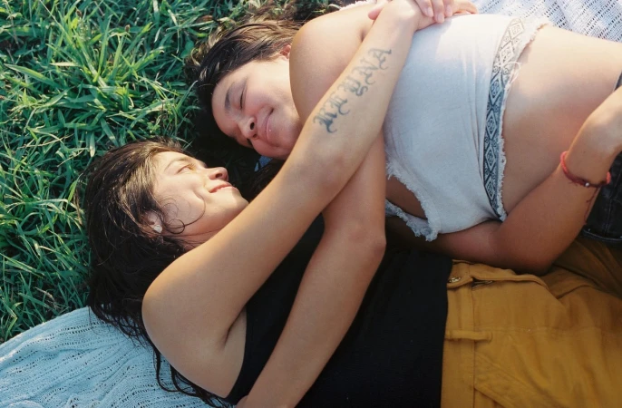 Two young women lying and embracing on a grassy meadow, captured in natural daylight by photographer Devyn Galindo