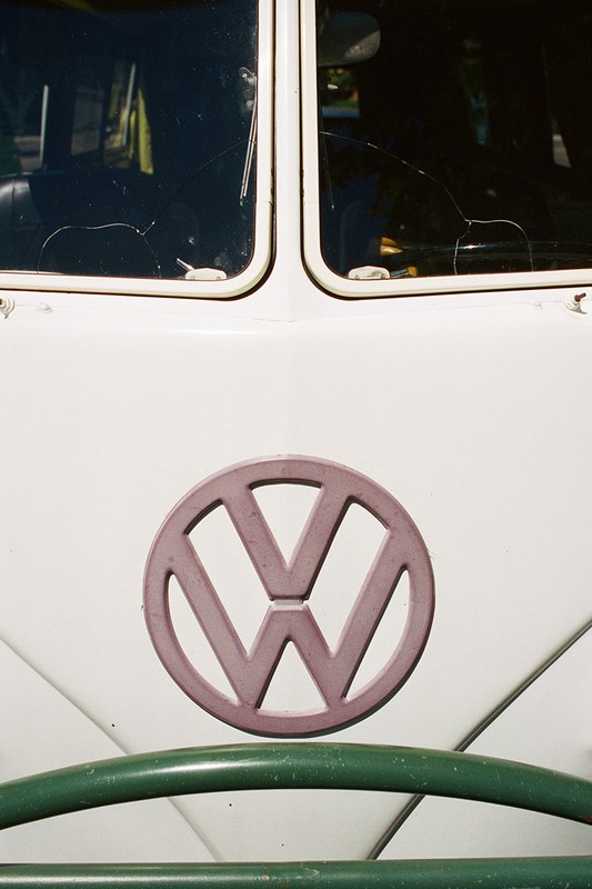 Close-up of a vintage Volkswagen van featuring the VW logo, windshield with cracks, white paint, and a green steering wheel.
