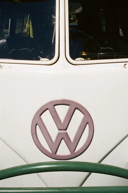 Close-up of a vintage Volkswagen van featuring the VW logo, windshield with cracks, white paint, and a green steering wheel.