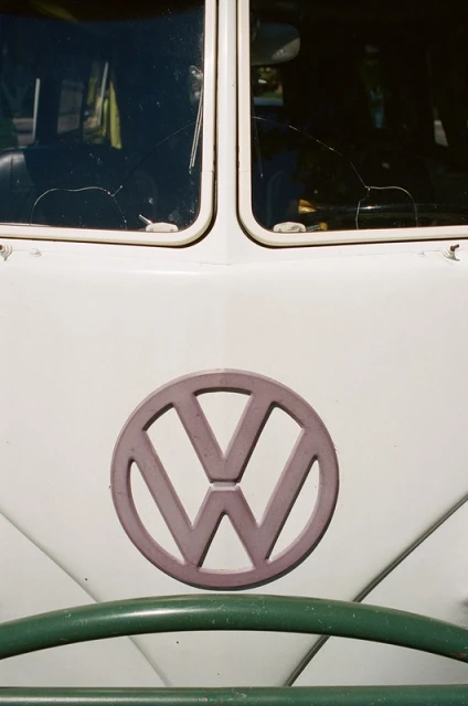 Close-up of a vintage Volkswagen bus with a white exterior, green bumper, and prominent VW logo, capturing a retro automotive aesthetic.