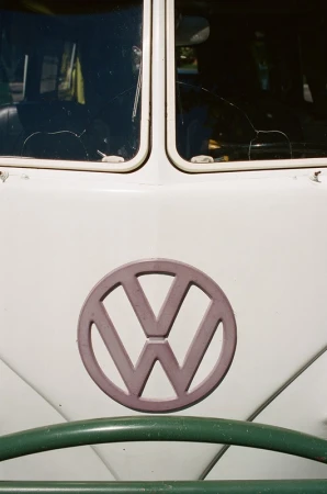 Close-up of a vintage Volkswagen bus with a white exterior, green bumper, and prominent VW logo, capturing a retro automotive aesthetic.