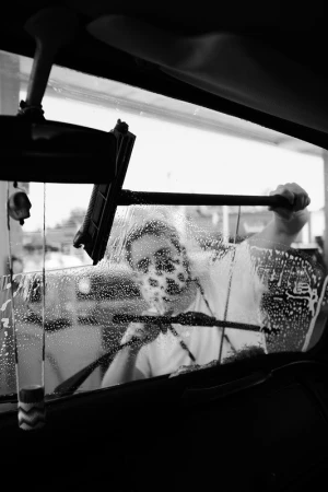 Monochrome shot through a car windshield as an adult cleans with soap and a squeegee for a clean view and safe driving.