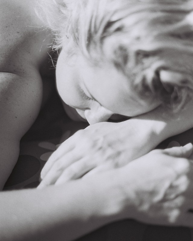 Close-up black and white portrait of an adult female resting her head on her folded hands; intimate, soft lighting, shallow depth of field.