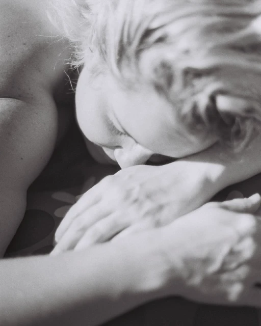 Close-up black and white portrait of an adult female resting her head on her folded hands; intimate, soft lighting, shallow depth of field.