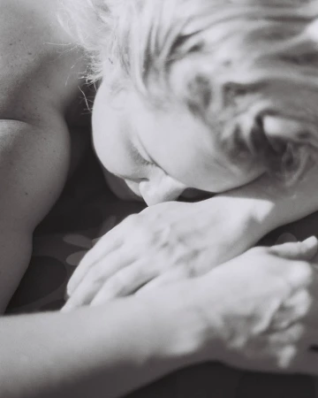Close-up black and white portrait of an adult female resting her head on her folded hands; intimate, soft lighting, shallow depth of field.