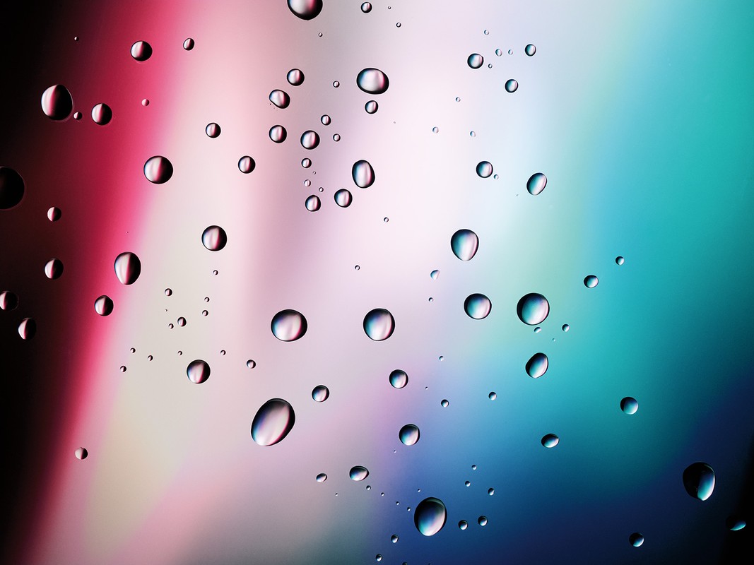 Macro photography captures a collection of water droplets clinging to a glass surface with blurred, colorful background.