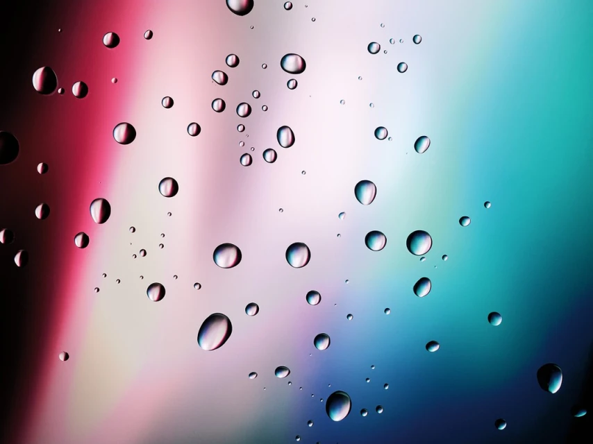 Macro photography captures a collection of water droplets clinging to a glass surface with blurred, colorful background. 