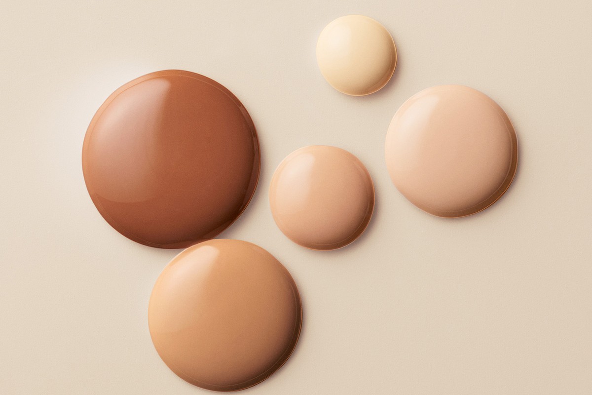 Five drops of different shades of foundation arranged on a light beige background, ranging from light to dark tone. Beauty concept.