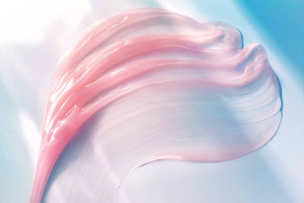 Close-up of a pink and white creamy cosmetic product swatch on a light blue background, highlighting its smooth texture and pearlescent sheen.