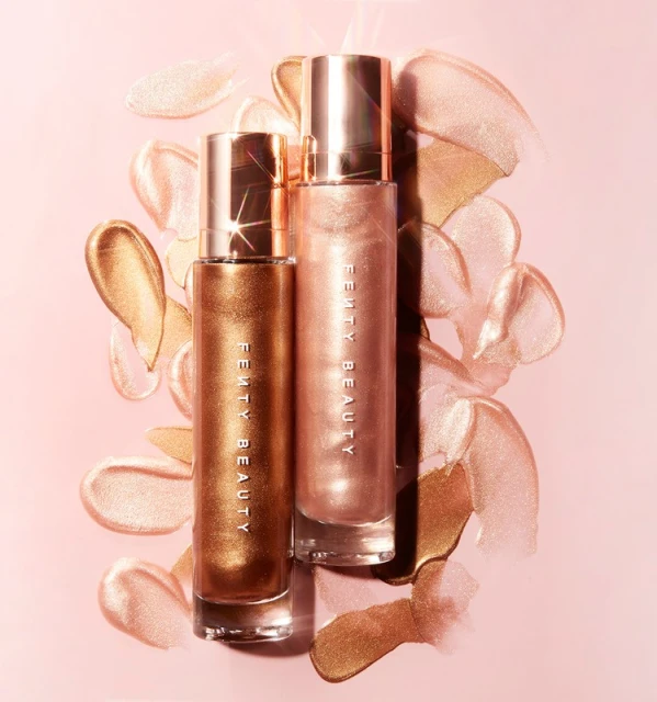 Two bottles of Fenty Beauty Body Lava luminizer on a pink background, surrounded by swatches of shimmery bronze and gold product.