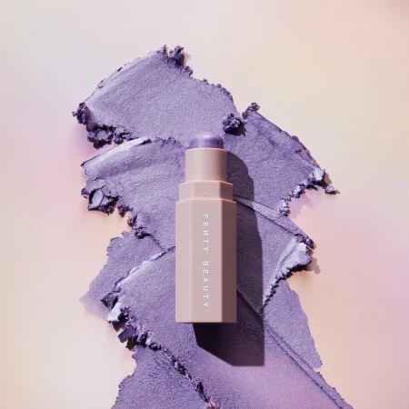 Fenty Beauty Match Stix Cream Shimmer with a swipe of shimmery purple eye shadow on a gradient peach to lavender background.