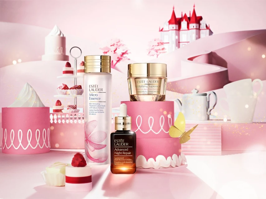 Still life shot of Estee Lauder skincare products arranged on tiered cake stands and pink platforms, with a decorative castle backdrop.