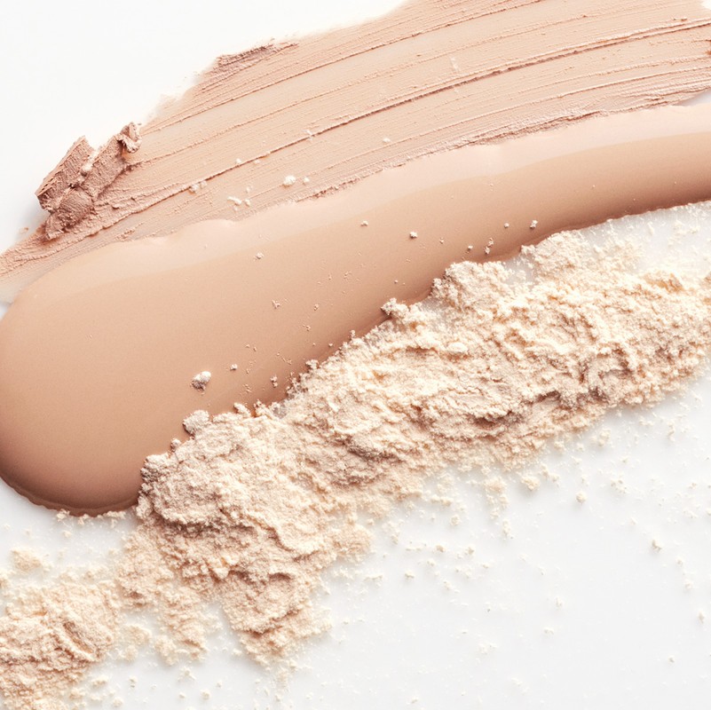 Close-up shot of foundation, concealer, and powder makeup swatches in neutral tones against a clean white backdrop.
