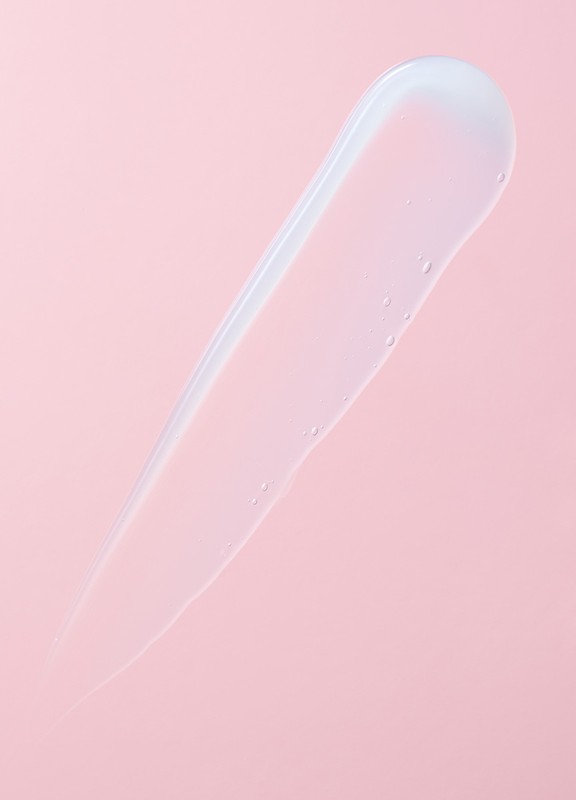 Clear gel serum skincare swatch on a pink background. Minimalist beauty and cosmetic product photography for skin treatment ad campaign.