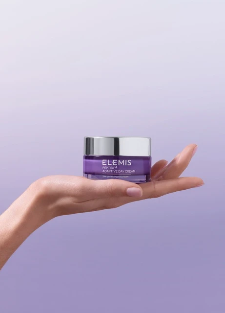 Elegant skincare product, Elemis Peptide4 Adaptive Day Cream, presented on a woman's palm against a soft purple gradient backdrop.