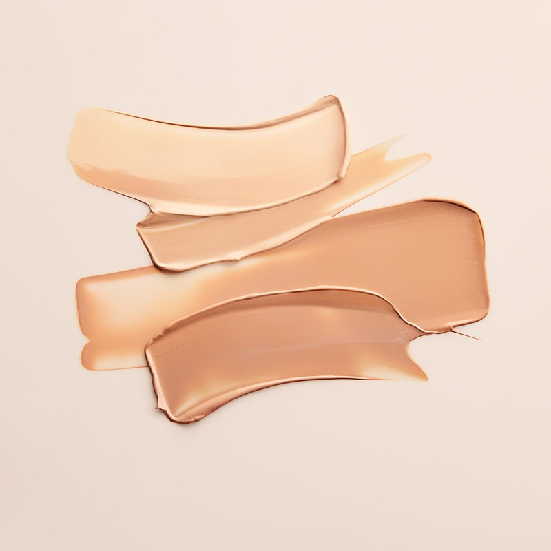 Close-up of foundation swatches in light to medium shades. Creamy texture on a neutral background in a horizontal, eye-level shot.