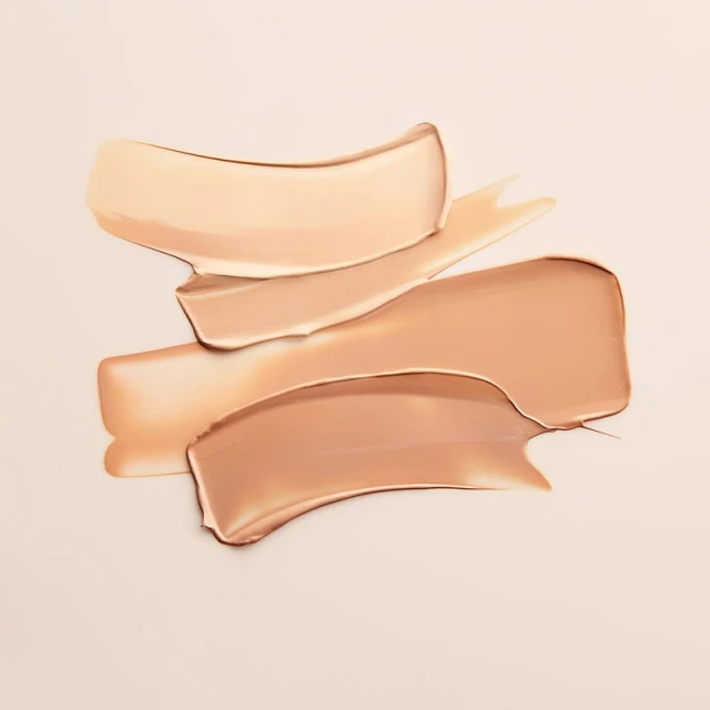Close-up of foundation swatches in light to medium shades. Creamy texture on a neutral background in a horizontal, eye-level shot.