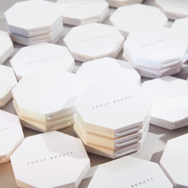 Cosmetic product flat lay. Multiple octagonal white Fenty Beauty compacts arranged on a surface, some stacked, showcasing makeup.