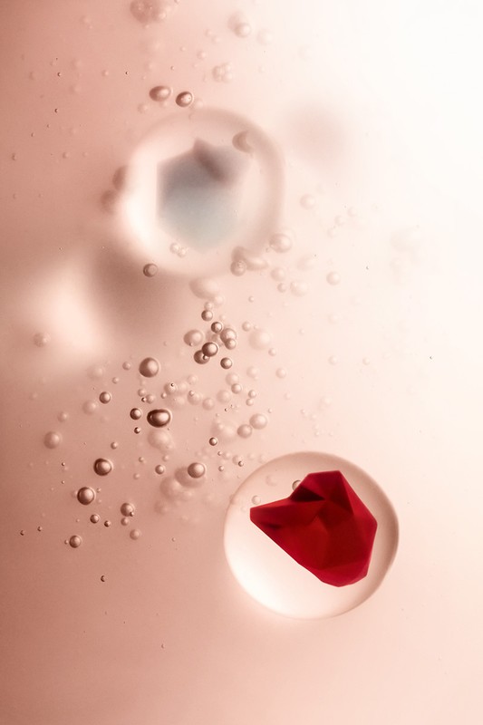 Abstract image featuring a red petal enclosed in a clear bubble and smaller transparent bubbles against a gradient pink background.