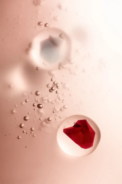 Abstract image featuring a red petal enclosed in a clear bubble and smaller transparent bubbles against a gradient pink background.