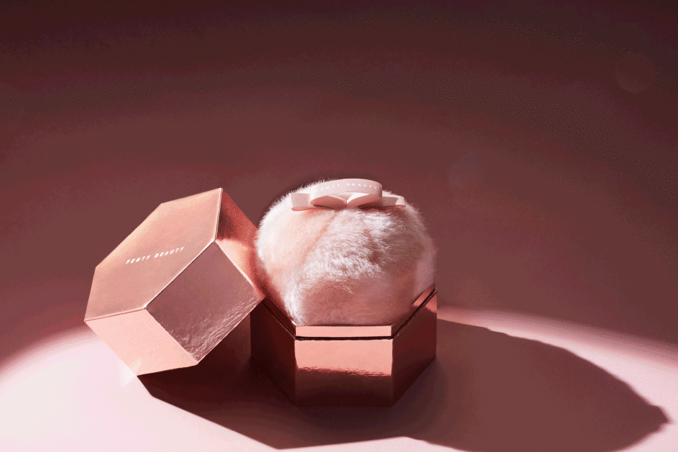 Fenty Beauty powder puff sits inside a hexagonal container with an open lid on a monochromatic background in a beauty studio setting.