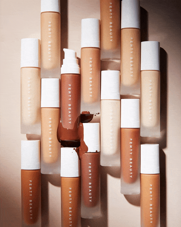 Overhead shot of Fenty Beauty foundation bottles in varying shades, arranged on a beige surface, capturing a beauty and cosmetic product scene.