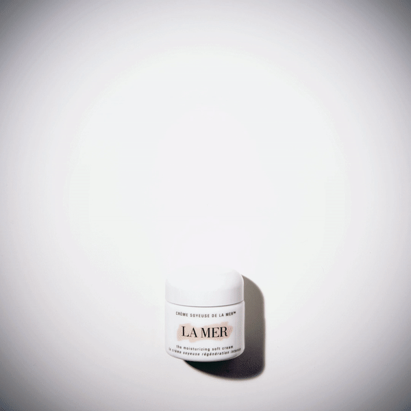 Close-up of a white jar of La Mer moisturizing cream on a white surface, captured with soft, diffused lighting and minimal composition.
