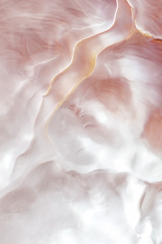 Abstract aerial view of pale pink and white landscape with fluid-like patterns and flowing, curving lines; organic and flowing forms.