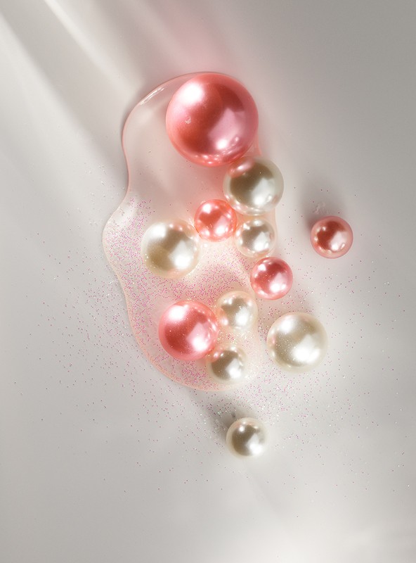 Close-up of a collection of pearl-colored and pink spheres and droplets of liquid, creating a visually appealing abstract composition.