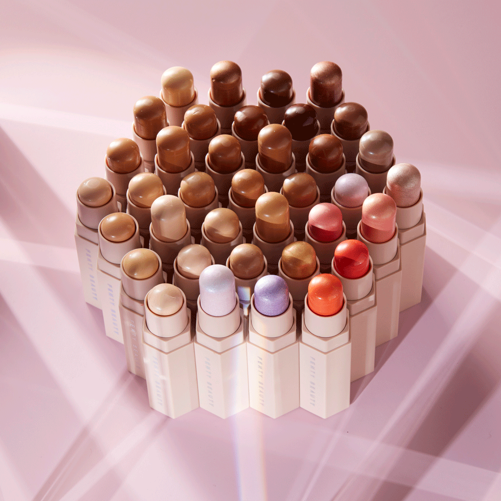 Cosmetic display featuring an array of Fenty Match Stix arranged in a hexagonal formation on a soft pink surface, beauty products.