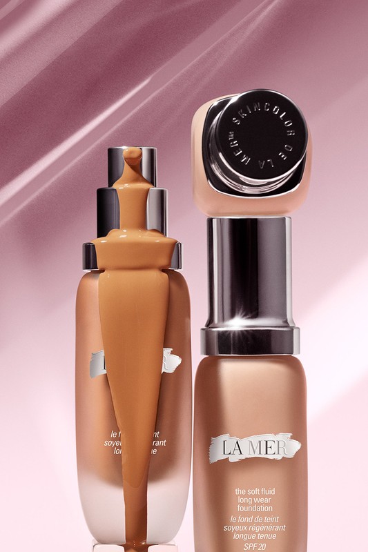 Two bottles of La Mer The Soft Fluid Long Wear Foundation displayed against a light pink background, highlighting the makeup product.