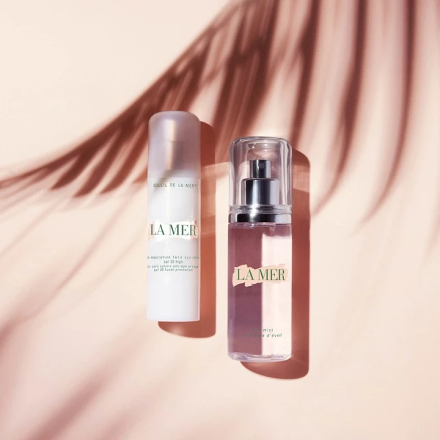 Two La Mer skin care bottles on a light peach surface with palm frond shadows create a calming and minimalist beauty aesthetic.