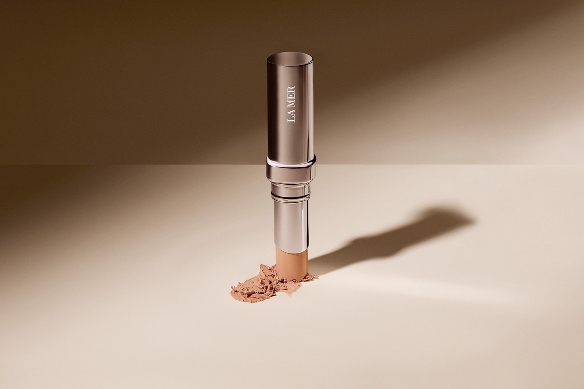Silver La Mer makeup stick with product smudge on beige backdrop, studio lighting, neutral palette, beauty product shot.