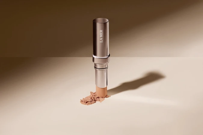 Silver La Mer makeup stick with product smudge on beige backdrop, studio lighting, neutral palette, beauty product shot.