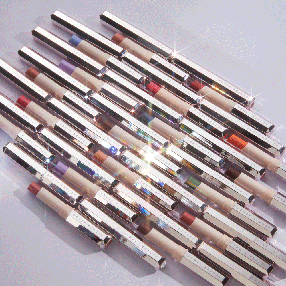 Arrangement of Fenty Beauty makeup sticks in varying shades on a white surface with studio lighting, highlighting product textures and colors.